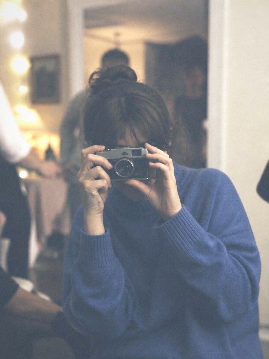 A person raising a small film camera to their eye at a gathering
