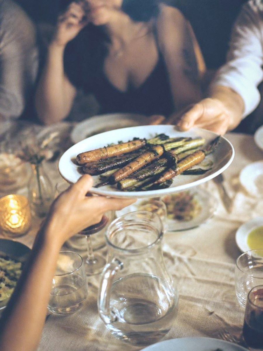 Hands passing a plate of shared food across a long table